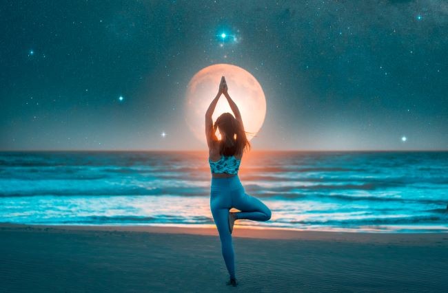 fata care face yoga la malul unei ape in timp ce priveste cerul colorat si cu luna plina