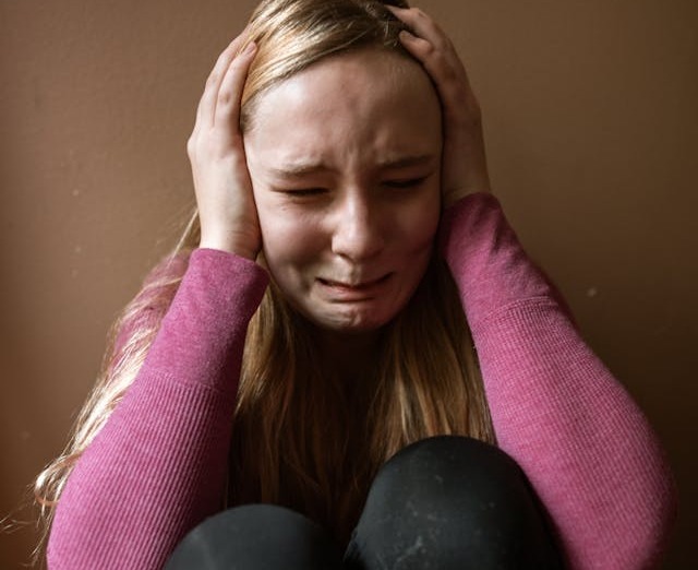 Fată care plânge și are mâinile pe urechi 