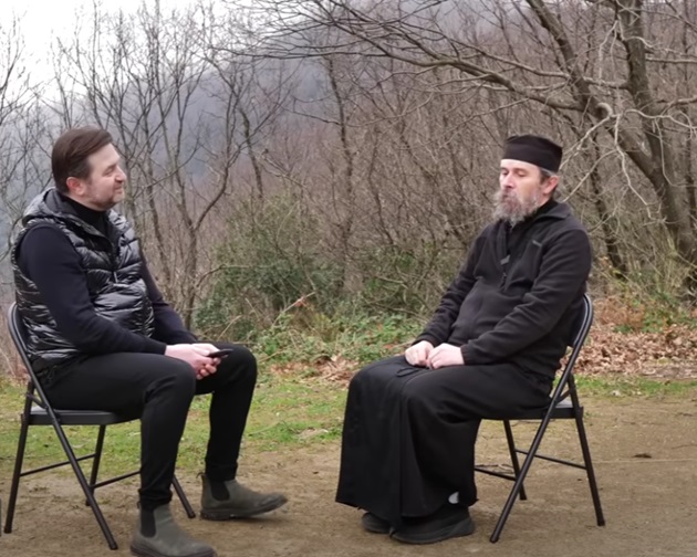Părintele Teologos și jurnalistul Adrian Artene stând de vorbă pe Muntele Athos, așezați față în față pe scaune negre pliabile, îmbrăcați amândoi în haine negre