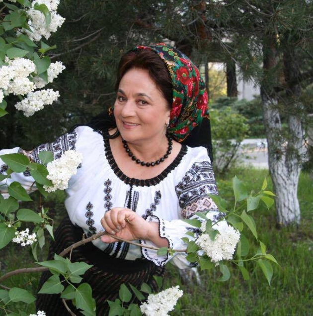 laura lavric imbracata in costum popular pozeaza in aer liber langa o tufa de liliac alb