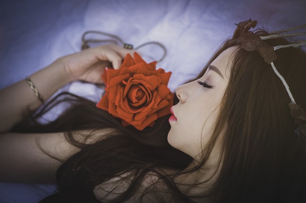 Femeie care stă întinsă în pat și miroase un trandafir.