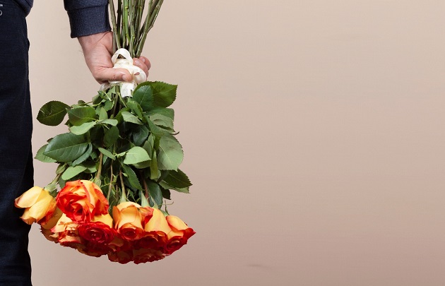 Bărbat care ține în mână un buchet de trandafiri portocalii.