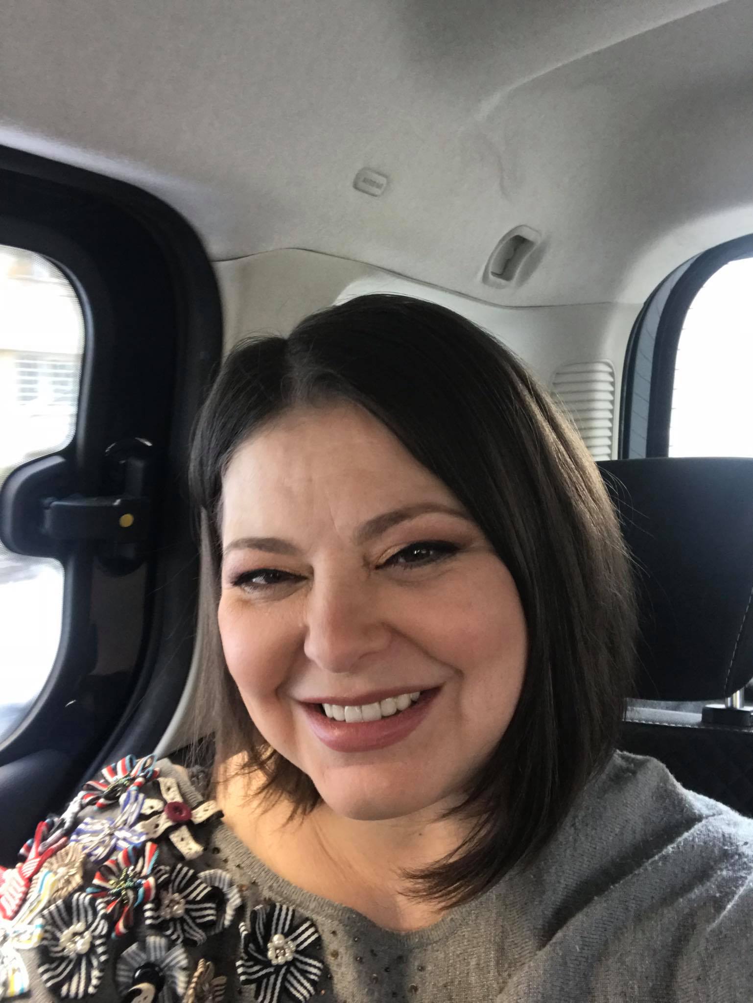 Rita Mureșan zâmbitoare, făcându-și un selfie în mașină, în timp ce era tunsă până la umăr și purta un pulover gri cu flori